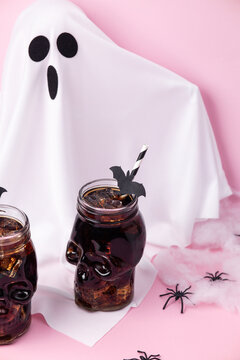 Ghost costume with skull drinks and Halloween spider decorations on pink background