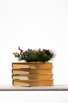 Cozy holiday book stack with evergreen wreath and red berries on a wooden table. Perfect for winter reading sales, Christmas gift guides, and bookstore promotions. High-quality festive atmosphere.