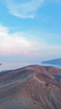 Volcanic Island Landscape with Crater Foreground Over Calm Sea Under Soft Blue Sky. Drone shot of Mount Krakatoa