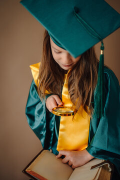 Child student graduating exploring book with magnifying glass