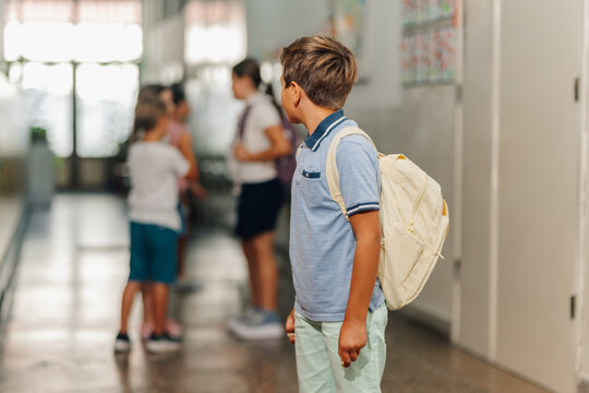 Boy standing alone in school hallway observing other students