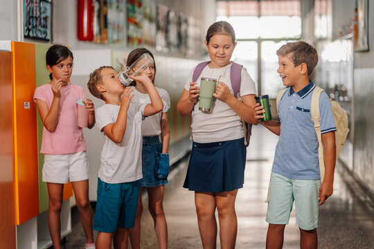 School children hydrating in corridor carrying reusable bottles
