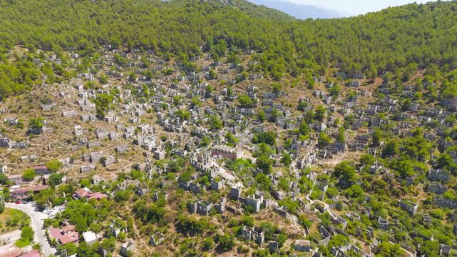 Kayakoy, Turkey. Abandoned ghost town ruins of hundreds of stone houses cascading down mountain slopes under bright sun, wide aerial drone view. Aerial View, Departure of the camera