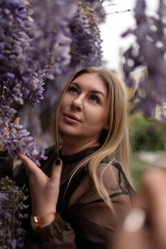 Blonde woman gently touching blooming purple wisteria flowers in a tranquil spring garden