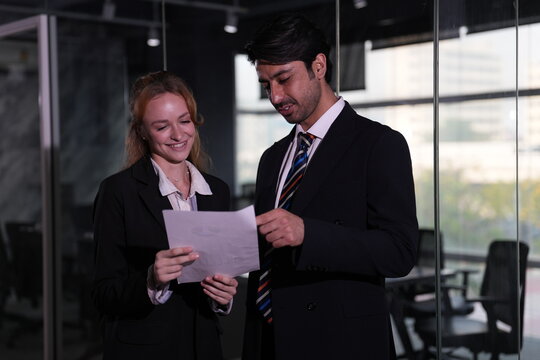 Ginger haired professional takes hold of the document with both hands as her dark haired colleague leans in to reread a line in the bright glass fronted office in a bright modern coworking.