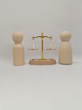 Two wooden figures beside golden balance scale symbolizing equality, fairness and impartial justice in human relationships and society between different gender. Business concept background