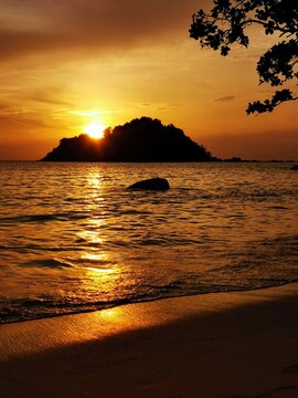 sunset over the sea. Golden sunset over ocean horizon with island silhouette reflecting warm light across tranquil waves and shoreline