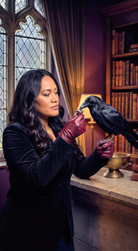 Woman in black velvet jacket and leather gloves feeding black raven perched on her hand in gothic library. Female holding small dish for crow near arched window with halloween aesthetic mood