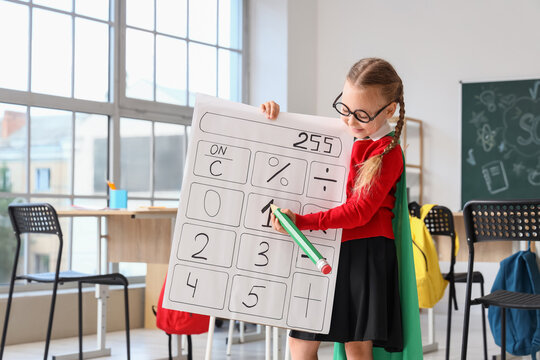 Stem education and math learning, young girl dressed as a superhero holding a large calculator poster in a classroom for academic development and growth