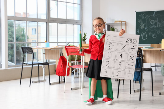 Stem education and math learning, schoolgirl dressed as a superhero holding a large calculator poster and pencil in a classroom for academic success
