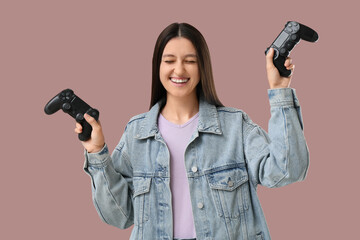 Gaming addiction and entertainment, happy young woman holding two game controllers with excitement and joy in a casual denim jacket on solid background © Pixel-Shot