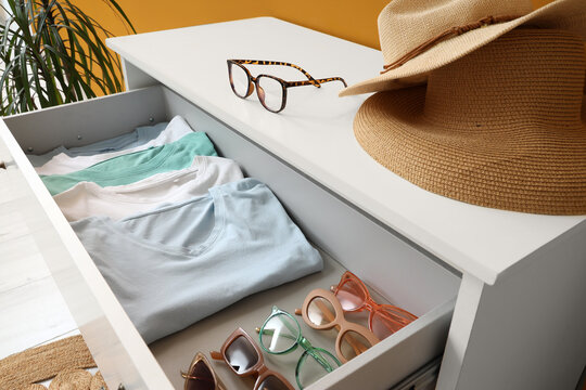 Organization and home storage, folded t-shirts in a dresser drawer with summer accessories and eyewear for a minimalist lifestyle and interior design