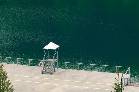 Aerial view of a lifeguard tower on a concrete pier next to a deep green lake