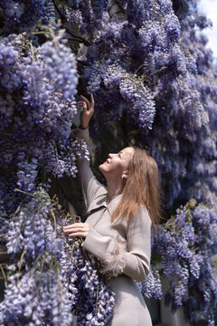 Woman touching purple wisteria flowers outdoors during a sunny spring day in a lush garden setting