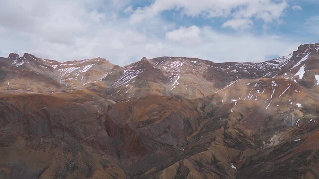 Wide angle shot of dry Himalayan mountain range with patches of snow on mountain peaks with clouds above them during the summer season as seen from Tanglang La on Leh Manali highway in Ladakh, India.