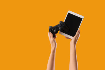 Woman holding game pad with blank tablet computer on yellow background © Pixel-Shot