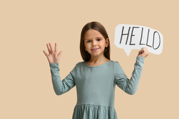 Cute little happy girl holding paper speech bubble with word HELLO while waving hand on beige background © Pixel-Shot