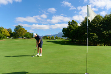 Obraz premium Man putting golf ball on green course near hole.