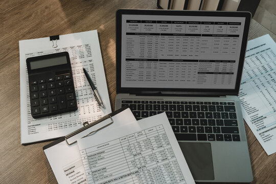 Laptop dashboard, calculator, financial reports, clipboard on desk for invoice review, receipt accounting, cash flow analysis, bookkeeping, business finance reporting.