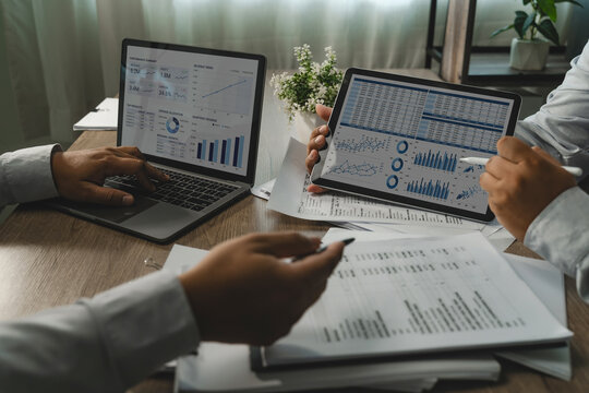 Two businessmen discussing spreadsheet tables and charts on laptop and tablet during business meeting for data analysis, financial reporting and performance review.
