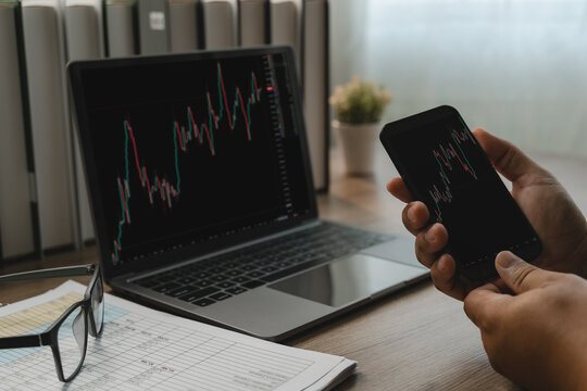Businessman Trading candlestick stock charts on smartphone and laptop graph stock market trading, showing mobile market analysis, online trading research and investment monitoring.