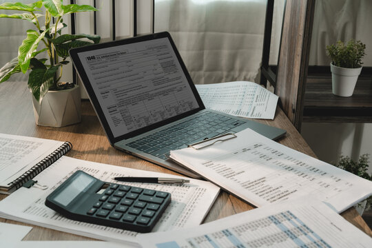 Tax preparation workspace with tax form on laptop, calculator and financial reports for accounting, tax season, audit, bookkeeping, financial planning.