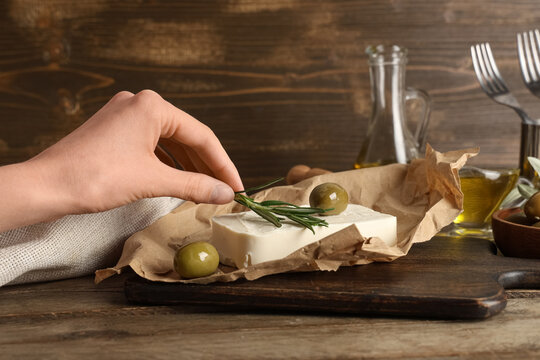 Female hand with tasty feta cheese, rosemary and olives on wooden background