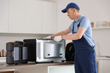 Male technician repairing electric oven in kitchen