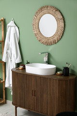 Obraz premium Modern sink with bath supplies on countertop and stylish mirror near green wall in bathroom
