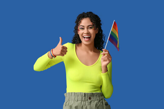 Happy African-American woman with rainbow flag showing thumb-up on blue background. LGBT concept