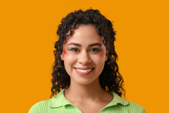 Young African-American woman with rainbow makeup on yellow background. LGBT concept