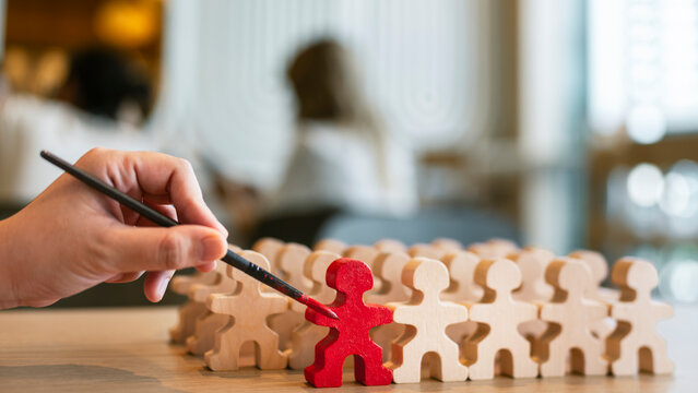 Talent recruitment and leadership concept with hand painting wooden figure in red among crowd on table for employee selection, career training, standout candidate and business development.