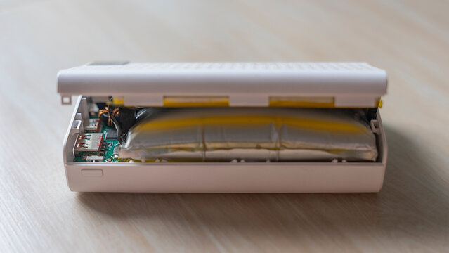 Swollen battery and electronic hazard concept with bloated power bank burst open on table showing dangerous lithium cell for hardware maintenance, device repair and e waste recycling.