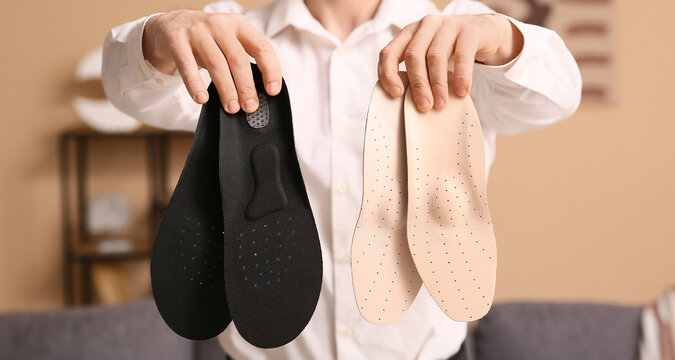 Orthopedic foot care and podiatry, person holding custom shoe insoles for arch support and pain relief in a clinical or home environment