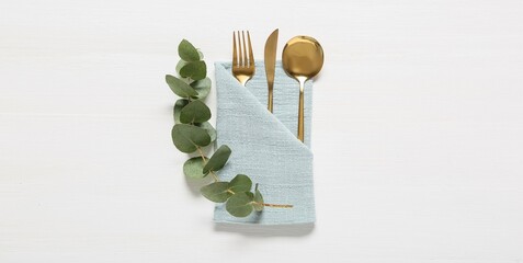Fine dining and hospitality concept, gold cutlery set with blue linen napkin and eucalyptus branch on a white wooden table for restaurant branding © Pixel-Shot