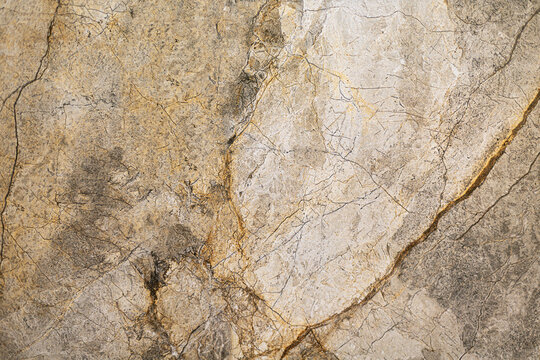 Beige and Gray Marble Stone Texture. Close-up of beige and gray marble with natural gold veining, fine cracks, mottled mineral patterns, and weathered stone texture.