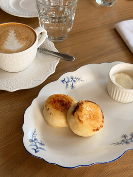 Breakfast at a caf&eacute;: syrniki (cottage cheese pancakes) with sour cream and a cappuccino, served on white porcelain tableware
