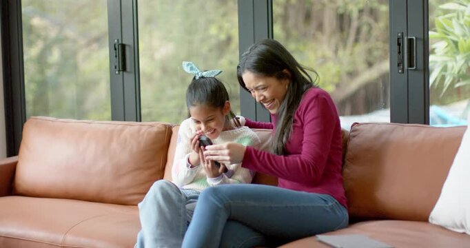 Mom and daughter sitting on couch at home, girl holding smartphone, mom teaching navigation