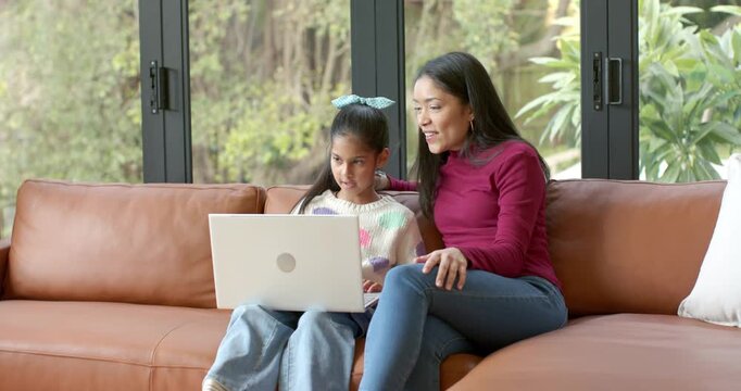 After opening laptop screen mother and daughter leaning on leather sofa exploring learning app