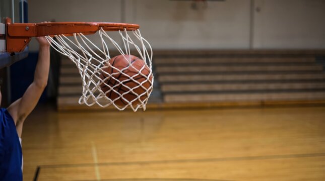 Basketball player dunking the ball through the hoop in an indoor gymnasium during a game action shot representing sports achievement, athletic power, and competition