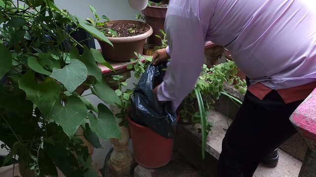 Hand Removing Paper Waste from Plant Pot into Black Trash Bag