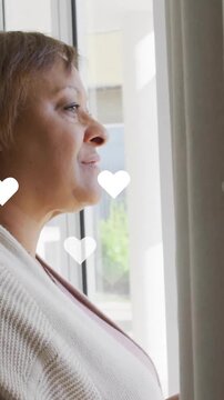 Woman looking out window with floating heart animations around her