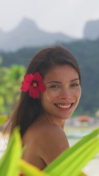 Beach beauty woman natural girl looking serene on tropical beach. Asian bikini model wearing hibicus flower body care wellness and spa pampering. Raw vertical video of real woman model without makeup