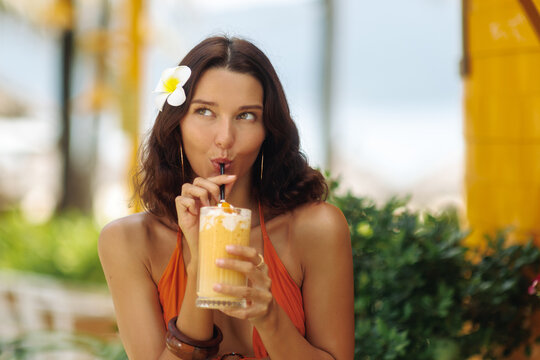 Young Woman Drinking Tropical Smoothie with Flower in Hair