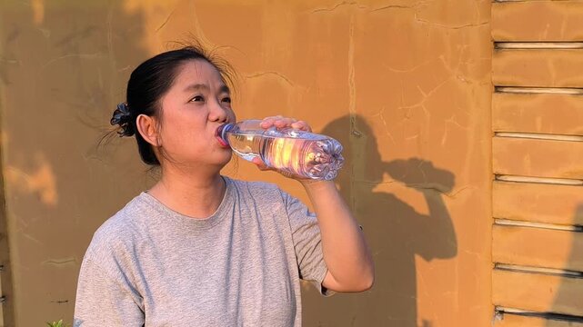 Asian woman drinking fresh water outdoors. An Asian woman quenches her thirst by drinking fresh water. Health campaign promoting hydration. Daily water intake and healthy lifestyle. 4k 60fps footage