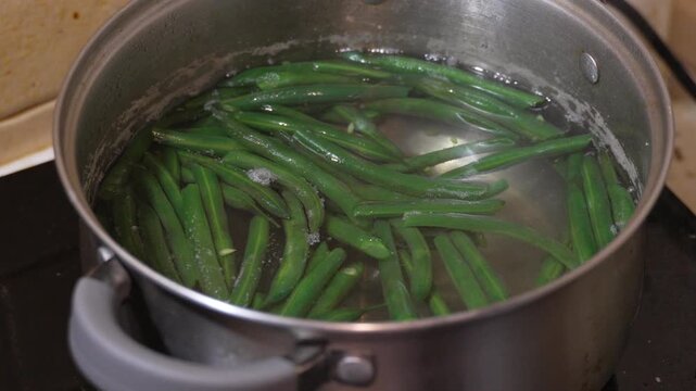 Boiling green beans being removed from hot water with metal tongs. Static camera shot capturing healthy home cooking food preparation process.