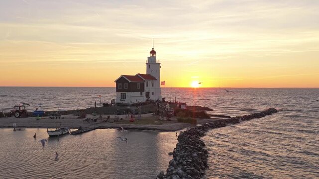 Golden sun setting over the calm sea next to the historic paard van marken lighthouse. Tourists admiring the iconic dutch landmark in holland
