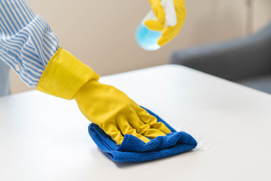 Close up of housekeeper in yellow gloves wiping table with microfiber cloth.