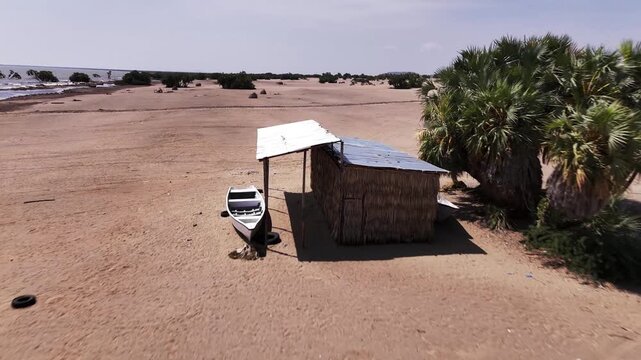 Aerial view of a lakeside shelter and small boat on the sandy shore of Lake Turkana, Kenya, surrounded by doum palms and arid terrain.