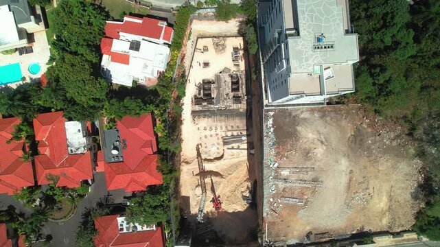 Top-down zenith aerial drone shot moving over a building construction site during foundation and drilling work next to residential houses and apartments